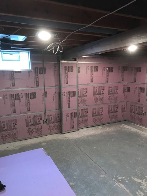A basement corner featuring pink foam insulation panels on concrete walls, exposed floor joists, and a window.