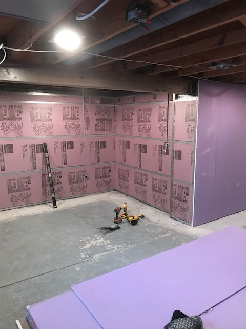 A basement under construction with pink rigid foam insulation boards on the walls and drywall boards on the floor.