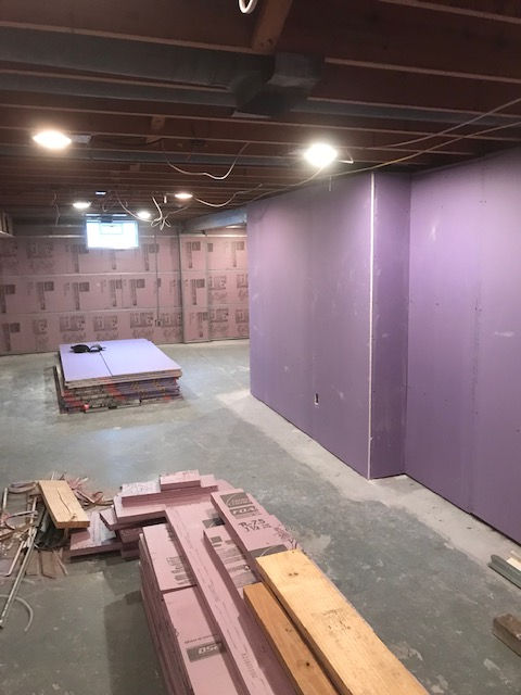 A basement under construction featuring purple drywall on a wall and stacks of pink rigid foam insulation on the floor.