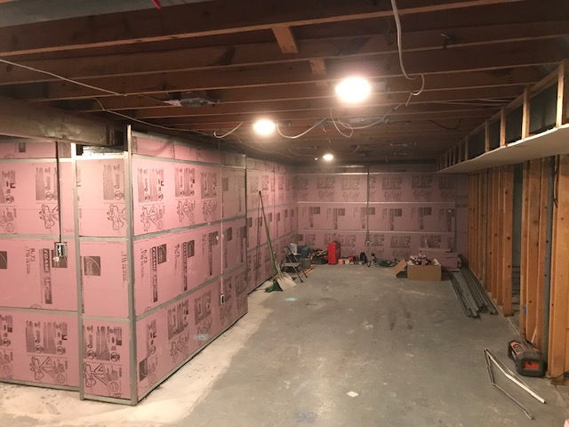 Unfinished basement with pink foam board insulation on concrete walls and exposed wooden ceiling joists.
