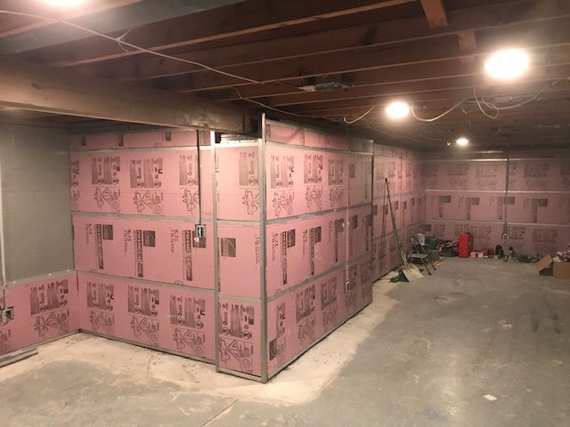 A basement interior with pink foam board insulation installed on the concrete walls.