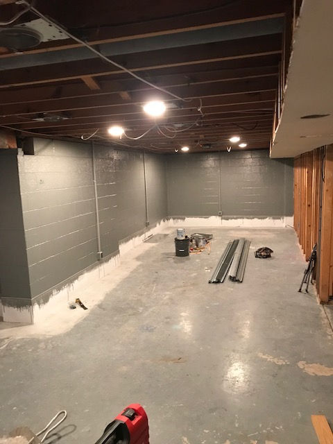 An unfinished basement room with freshly painted gray block walls, a concrete floor, and exposed ceiling joists.