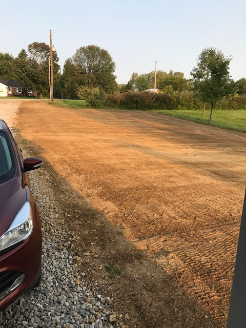 A red car parked next to a large area of bare, tilled soil on a bright day.