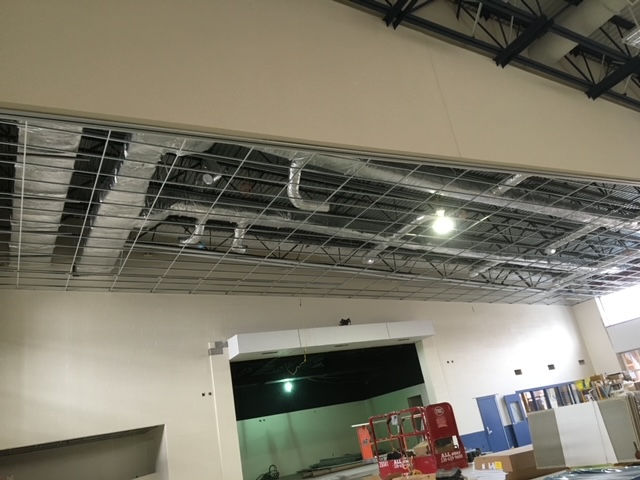 Open ceiling construction in a large room featuring a metal grid, ductwork, and steel joists.