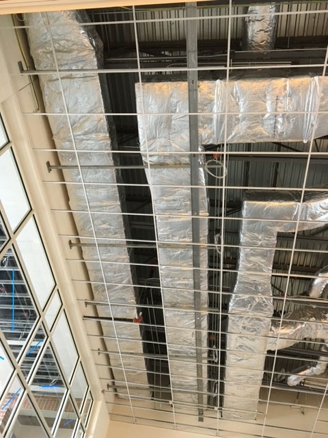 A view looking up at a metal grid ceiling structure with silver insulated HVAC ducts running through the rafters.
