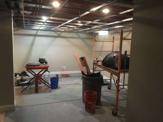 A basement renovation in progress, featuring a metal ceiling grid, a rolling scaffold, construction tools, and materials.