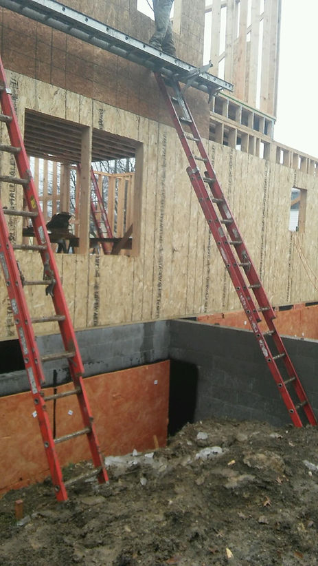 Two red extension ladders lean against the wood-framed wall of a residential construction site.