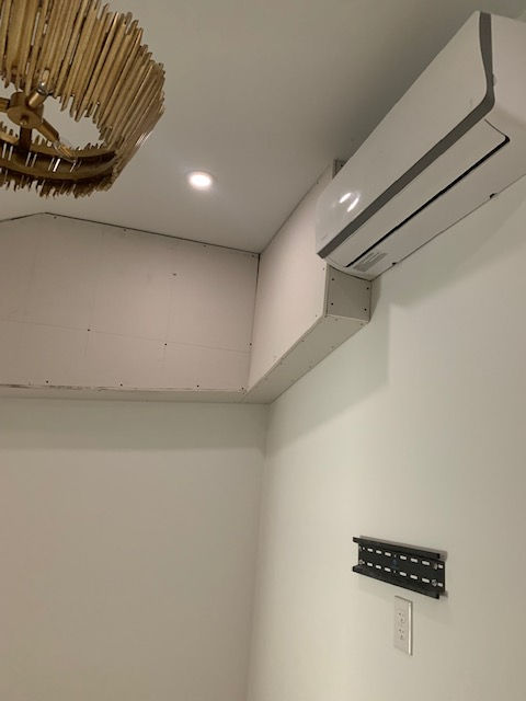 A white wall featuring a mounted air conditioner unit, a light fixture, and a TV wall mount bracket below.