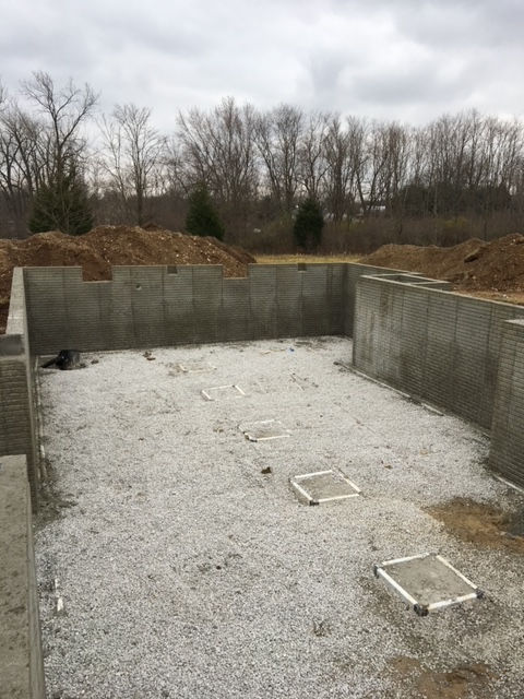 A construction site showing a poured concrete foundation and gravel-filled ground with square footings.