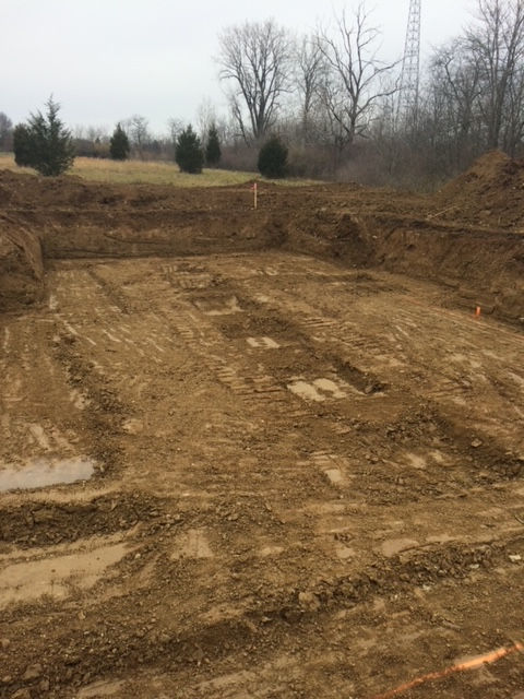 A muddy, excavated construction site showing trenching for a building foundation in a rural, open field.