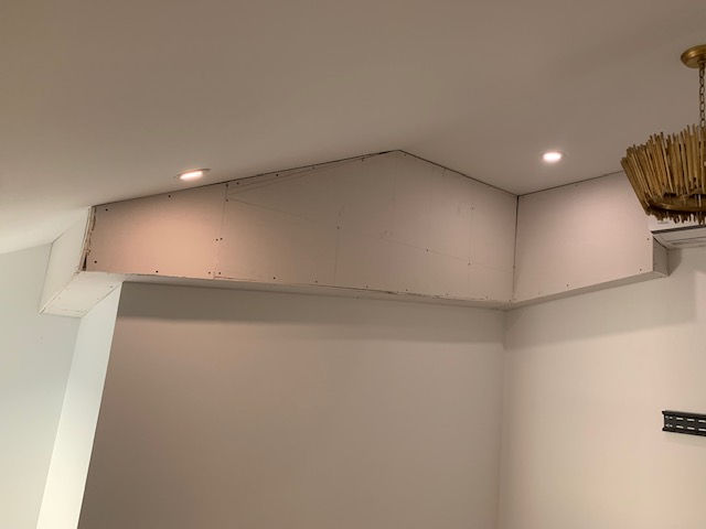Unfinished drywall structure on an interior wall with a vaulted ceiling, recessed lighting, and a hanging light fixture.