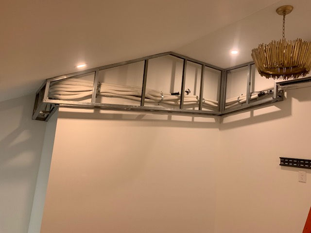 A metal wall frame is installed near the ceiling, containing white pipes and cables, against a plain interior wall.