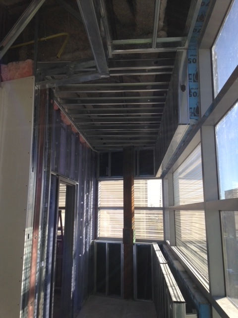 An interior view of a building under construction, featuring exposed metal framing, unfinished walls, and large windows.