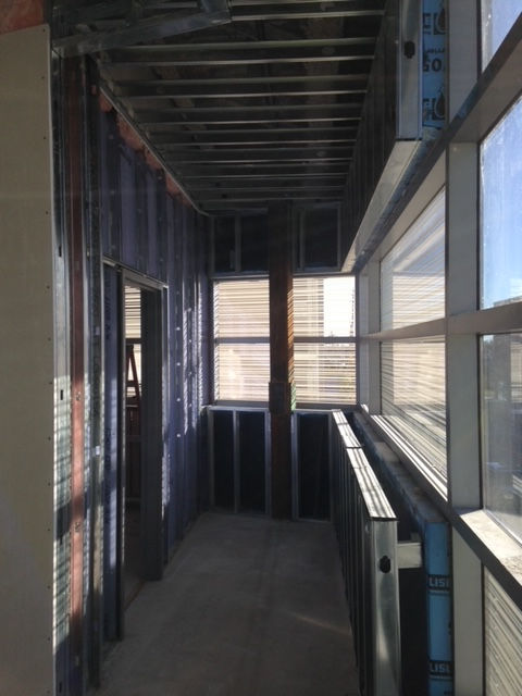 Construction site with metal framing, exposed ceiling joists, and a glass storefront window wall overlooking a exterior view.