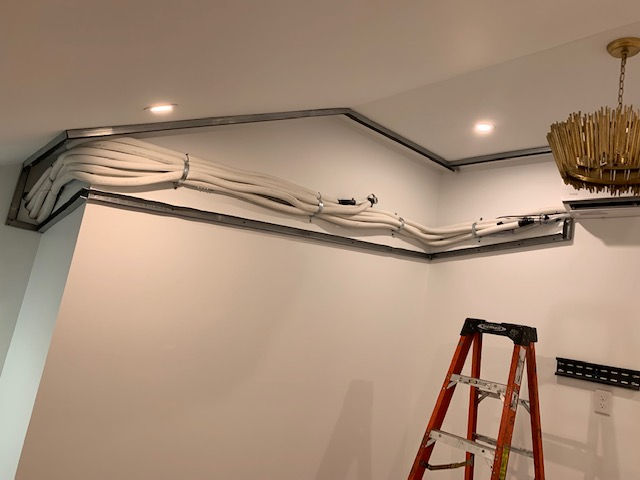 White HVAC refrigerant lines running along the top of an interior wall toward a ladder, with a gold chandelier nearby.
