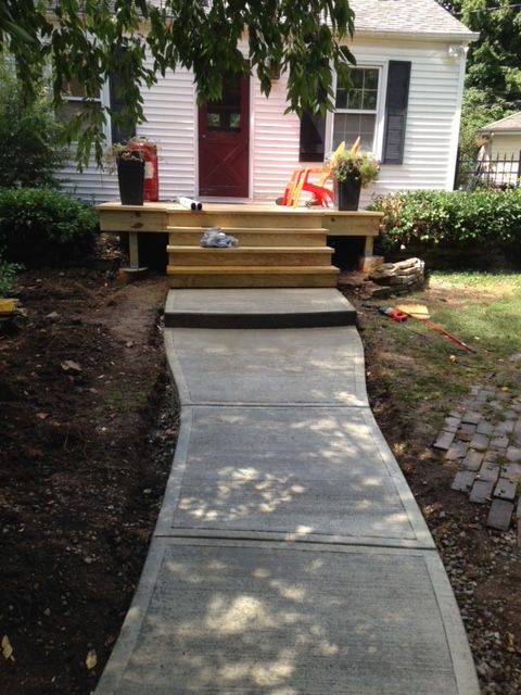 New wooden front porch steps lead up to a white house with a red door, connected to a concrete walkway in a yard.