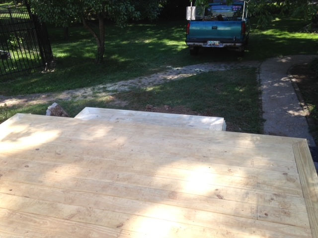 A view from a wooden deck under construction, overlooking a grassy yard with a parked truck in the background.