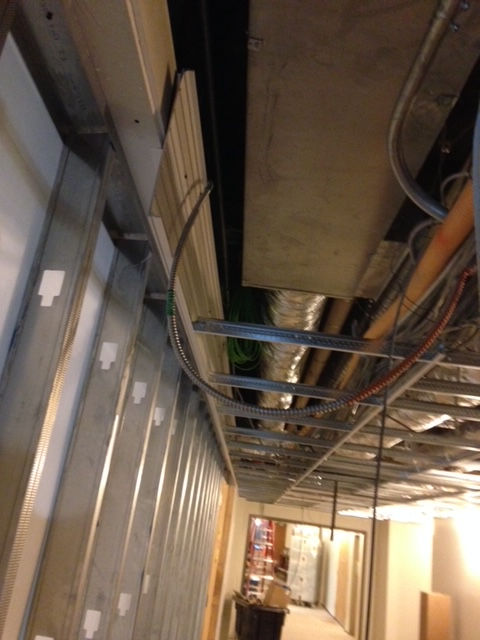 An interior construction site showing metal wall studs, exposed ceiling ductwork, and electrical wiring.