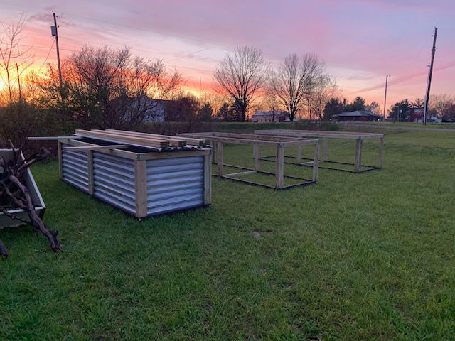 A corrugated metal planter box sits on a lawn next to wooden frames at sunset.