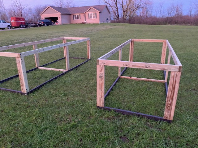 Two rectangular wooden frames sit on a grassy lawn in front of a house at dusk.