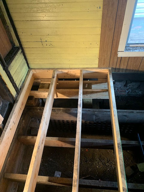 New floor joist framing installed against yellow wood walls in an unfinished home renovation.