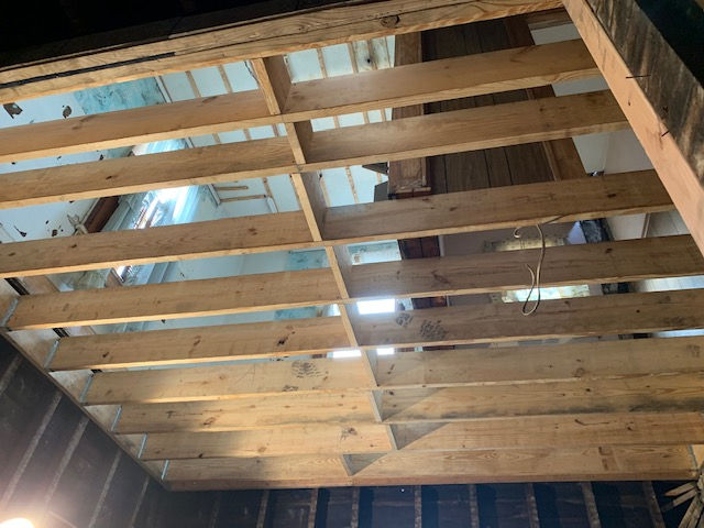 Looking up at newly installed light-colored wooden ceiling joists and framing in a room undergoing renovation.