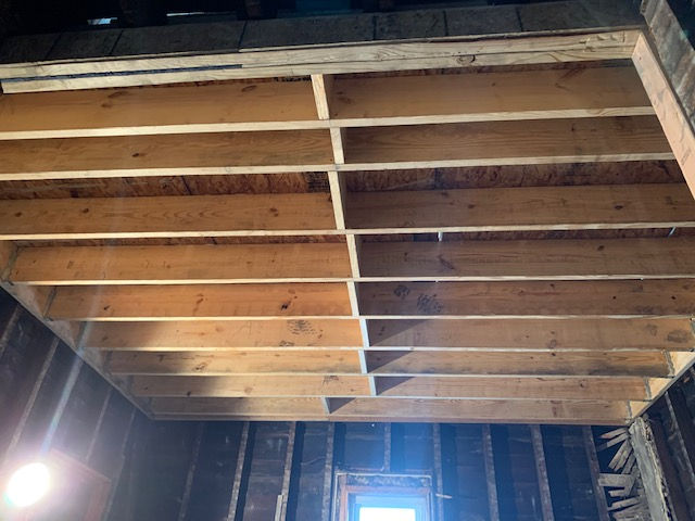 An unfinished ceiling interior showing exposed wooden joists and a plywood subfloor under construction.