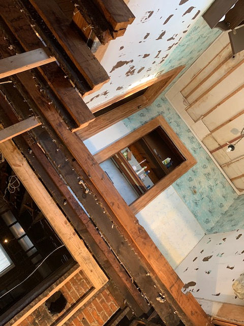 View from above of a room under construction, showing exposed wooden joists, peeling wallpaper, and a wooden doorway.