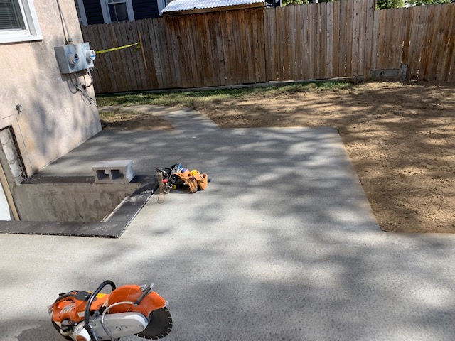 Newly poured concrete patio in a backyard with a circular saw in the foreground and a wooden fence in the background.