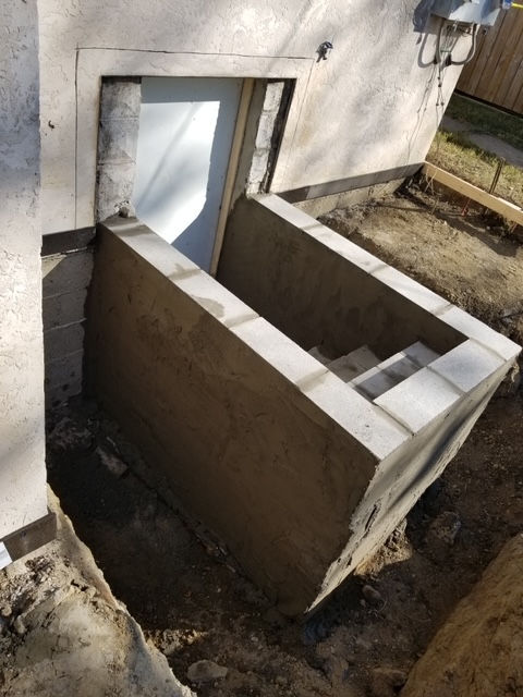 A basement walk-out staircase construction site featuring freshly parged concrete block walls leading to a doorway.