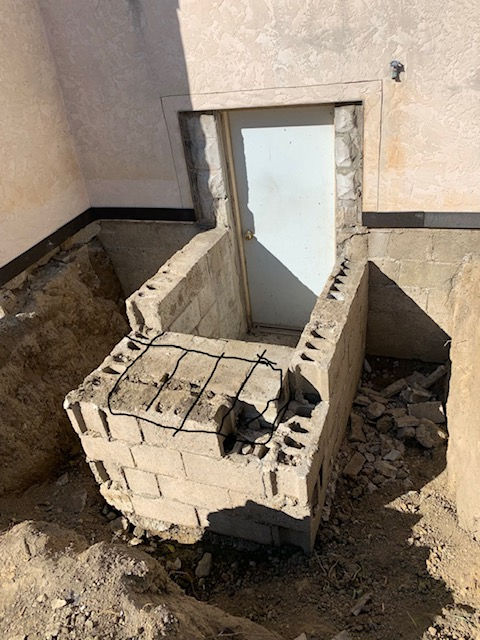 An unfinished cinder block staircase leading to a white door in a foundation excavation, surrounded by dirt.