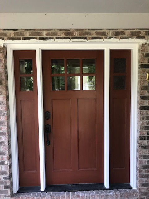 A reddish-brown front door with six window panes, flanked by two sidelights, set in a light brick wall.