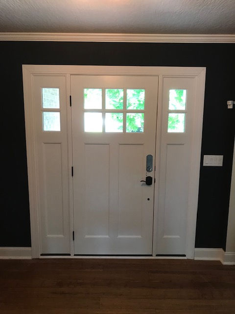 White front door with sidelights and glass panes, set against a dark wall in an interior foyer.