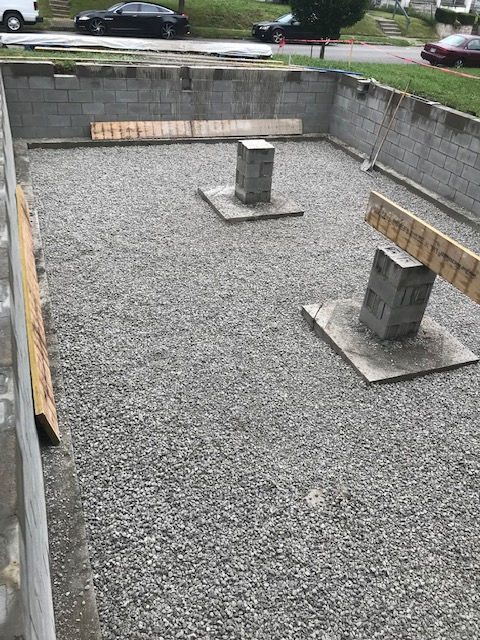 A construction site featuring a gravel-filled foundation, block walls, and two concrete support piers with wooden beams.