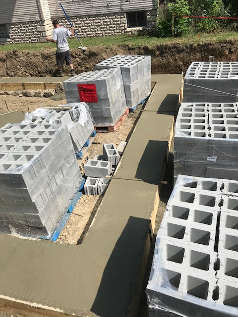 A person stands near stacks of concrete blocks placed on a newly poured concrete foundation at a construction site.