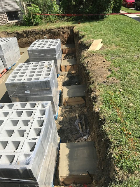 Construction site showing concrete block stacks placed beside a deep trench with evenly spaced, level concrete footings.