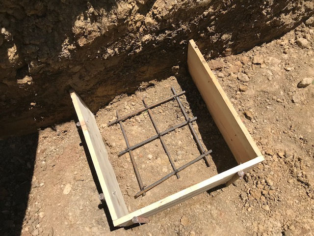 Wooden concrete forms placed in a dirt excavation with a steel rebar grid lying on the ground inside the frame.