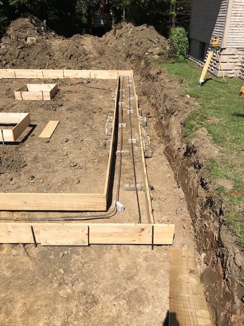 Wooden foundation forms and rebar reinforcement installed in an excavated trench at a construction site.