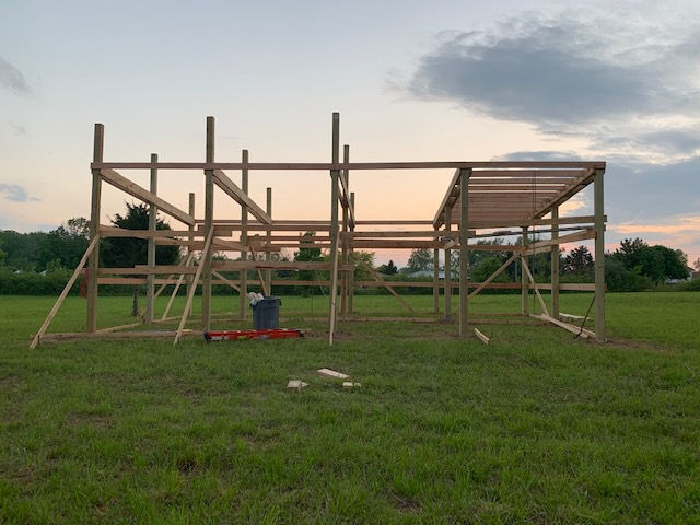 A wooden frame structure for a building under construction in a large, open grassy field at sunset.