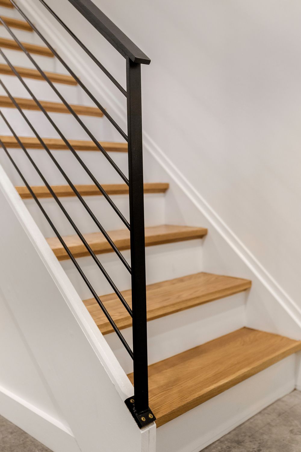 A staircase with light wood steps, white risers, and a black metal railing with horizontal bars.