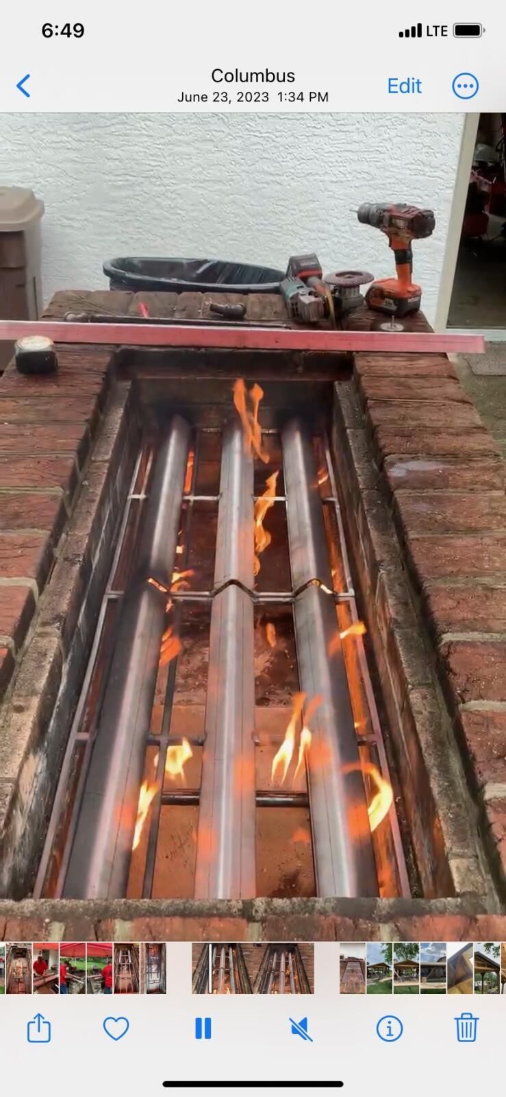 A brick outdoor fire pit with three parallel metal burner tubes glowing with orange flames.