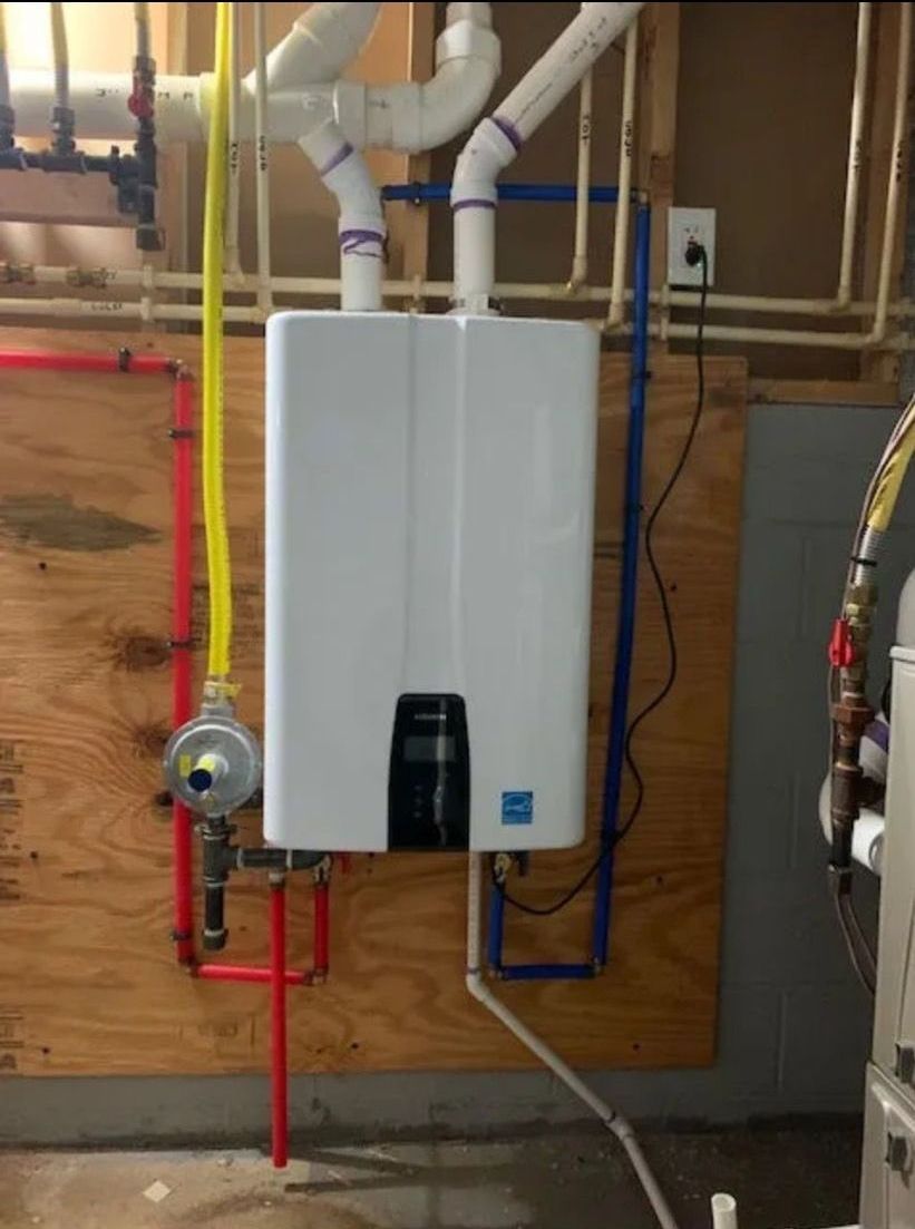 A white tankless water heater mounted on a wooden wall, connected to white vent pipes, gas lines, and red and blue water pipes.
