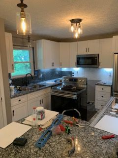 A kitchen renovation in progress, featuring white cabinets, granite countertops, a stove, microwave, and hanging lights.