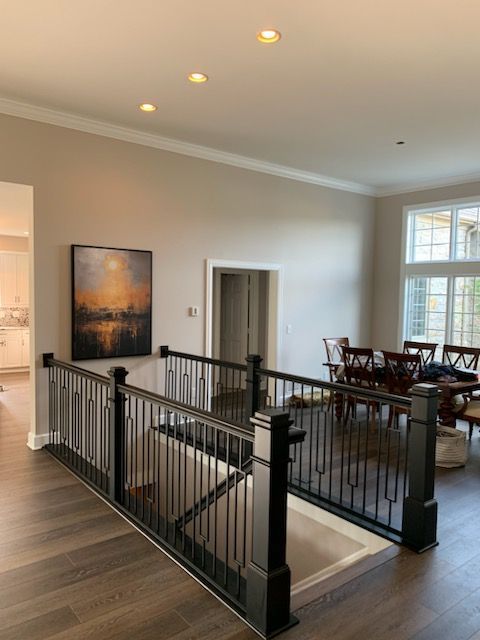 An interior view of a home showing a black staircase railing, hardwood floors, a framed art print, and a dining room.