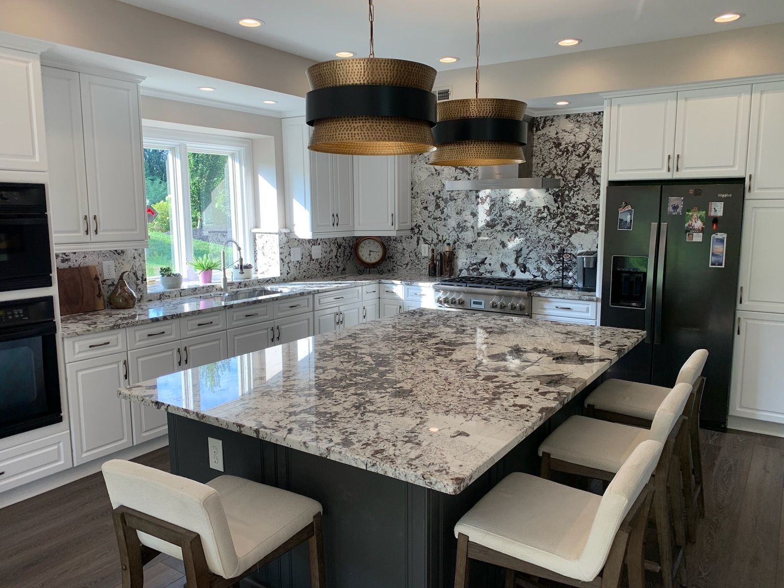 Modern kitchen with white cabinetry, a dark gray island with granite countertops, bar seating, and patterned backsplash.