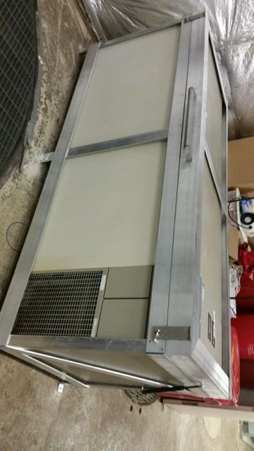 A chest freezer with a metallic frame, white side panels, and a vent on the lower corner, sitting in a storage space.