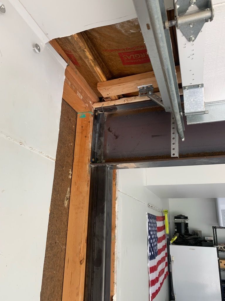 An interior view showing structural framing, an exposed steel beam, insulation, and garage door tracks in a home.