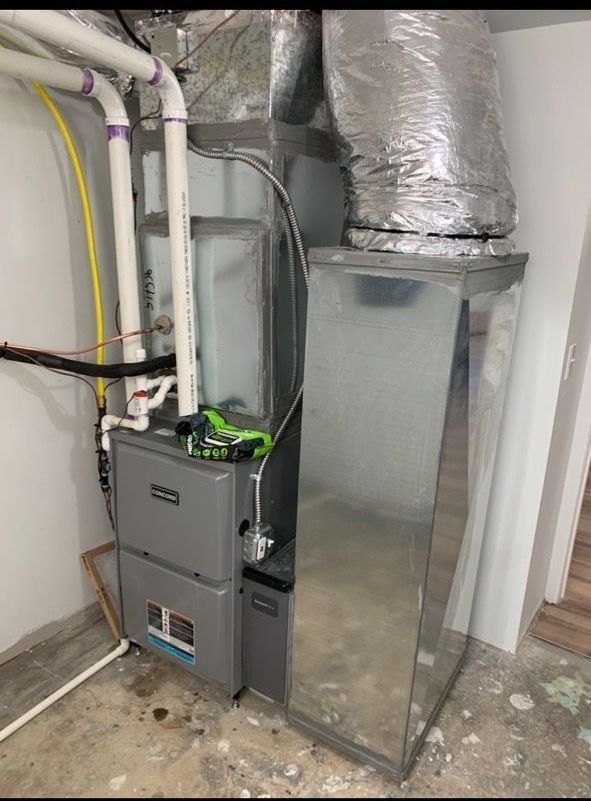 A vertical HVAC unit in a room with a concrete floor, featuring gray metal housing, white PVC pipes, and silver ductwork.
