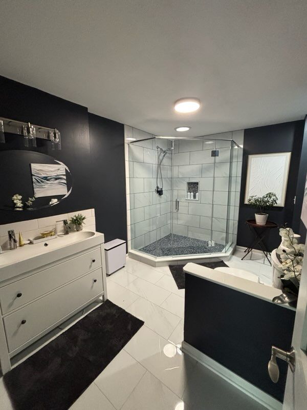Modern bathroom with dark navy walls, white vanity, glass corner shower, and glossy white tile floors.