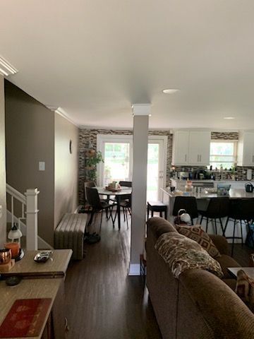 An open-concept living area with a brown sofa in the foreground, a dining area, and a kitchen with white cabinetry.